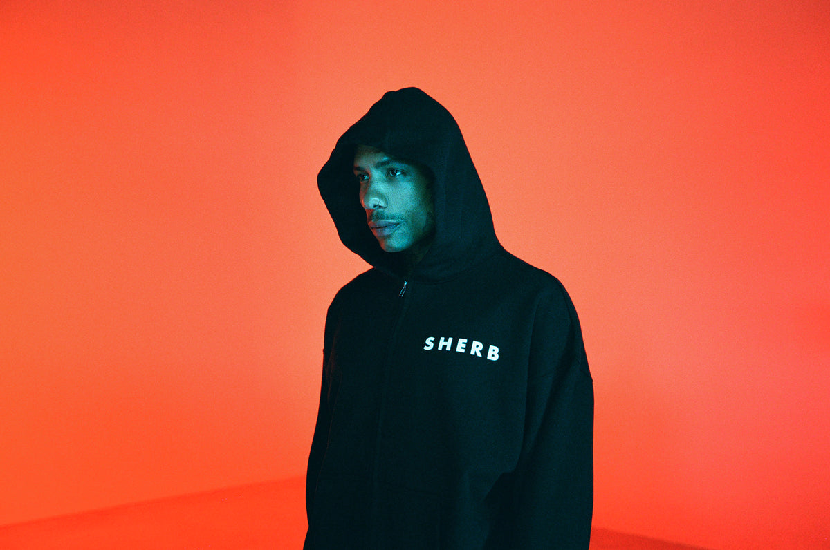 Black SHERB zip hoodie in an orange-lit studio